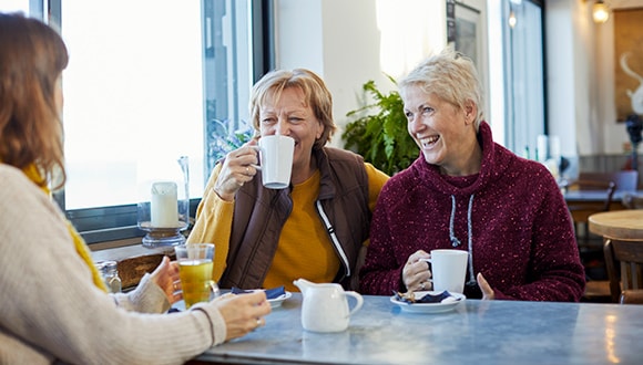 Three elderly females laughing over coffee