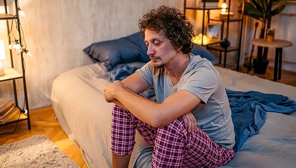 Man sitting on the edge of his bed feeling anxious at night