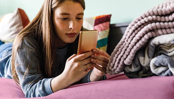 Young girl laying on her bed while looking at social media accounts